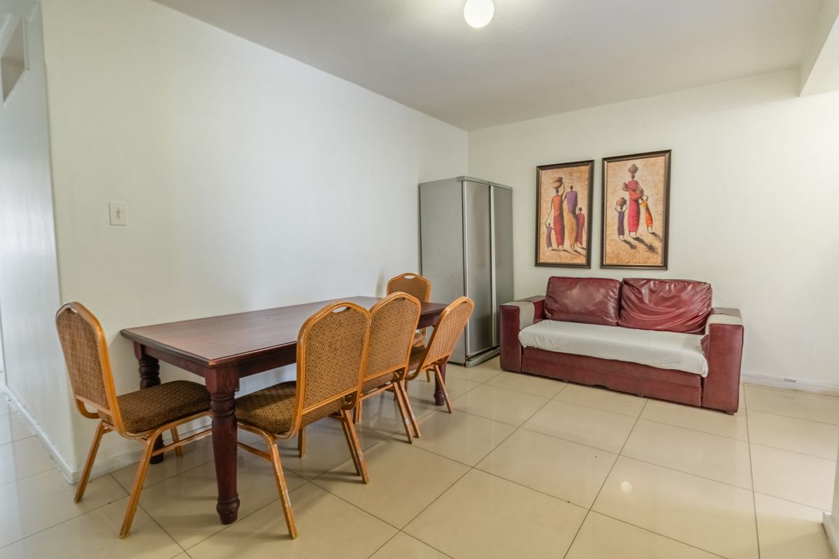 A functional living and dining area featuring neutral tiled flooring and plain walls, providing a versatile space for relaxation and meals.