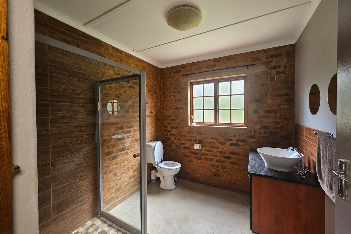 A rustic-style bathroom featuring exposed brick walls, a glass-enclosed shower, a vessel sink on a granite vanity, and a toilet.