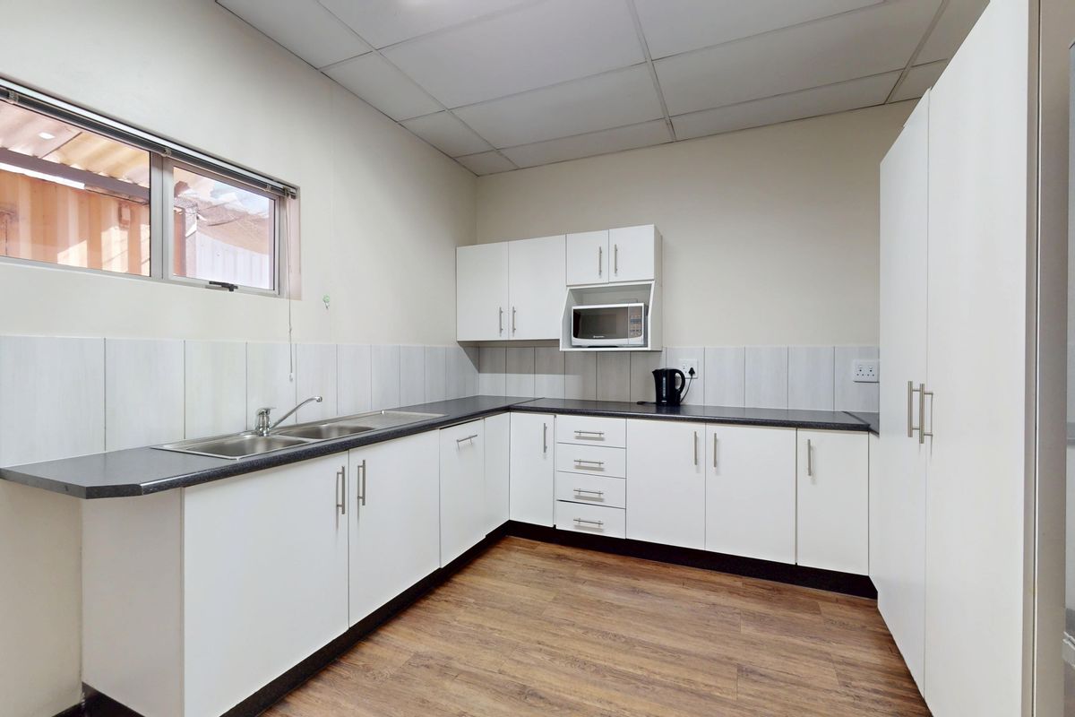 A clean and functional industrial kitchen featuring white cabinetry, dark laminate countertops, a stainless steel double sink, and durable vinyl flooring.