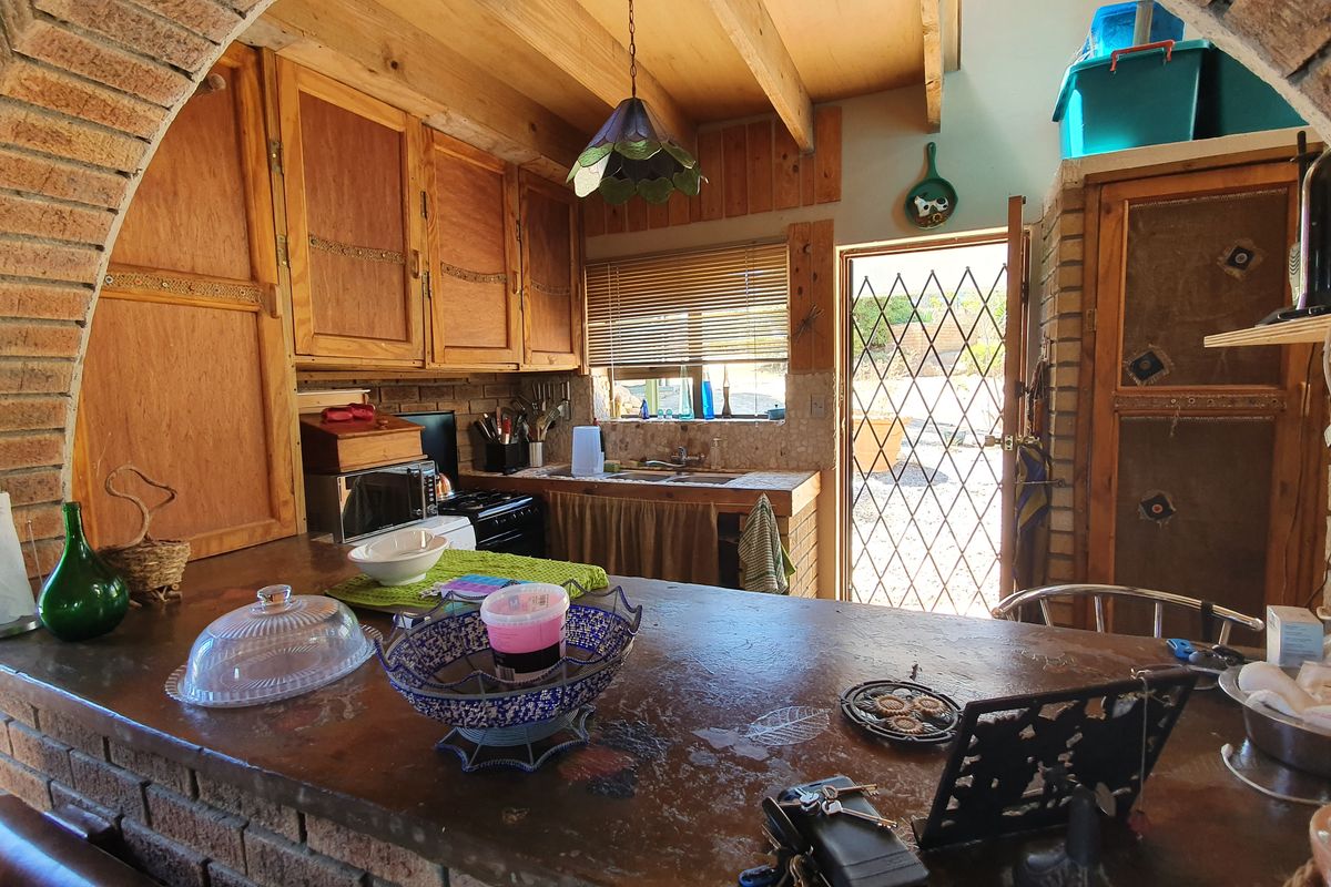 Rustic kitchen featuring exposed timber beams, a distinctive brick archway, wooden cabinetry, and direct access to the exterior through a security gate.
