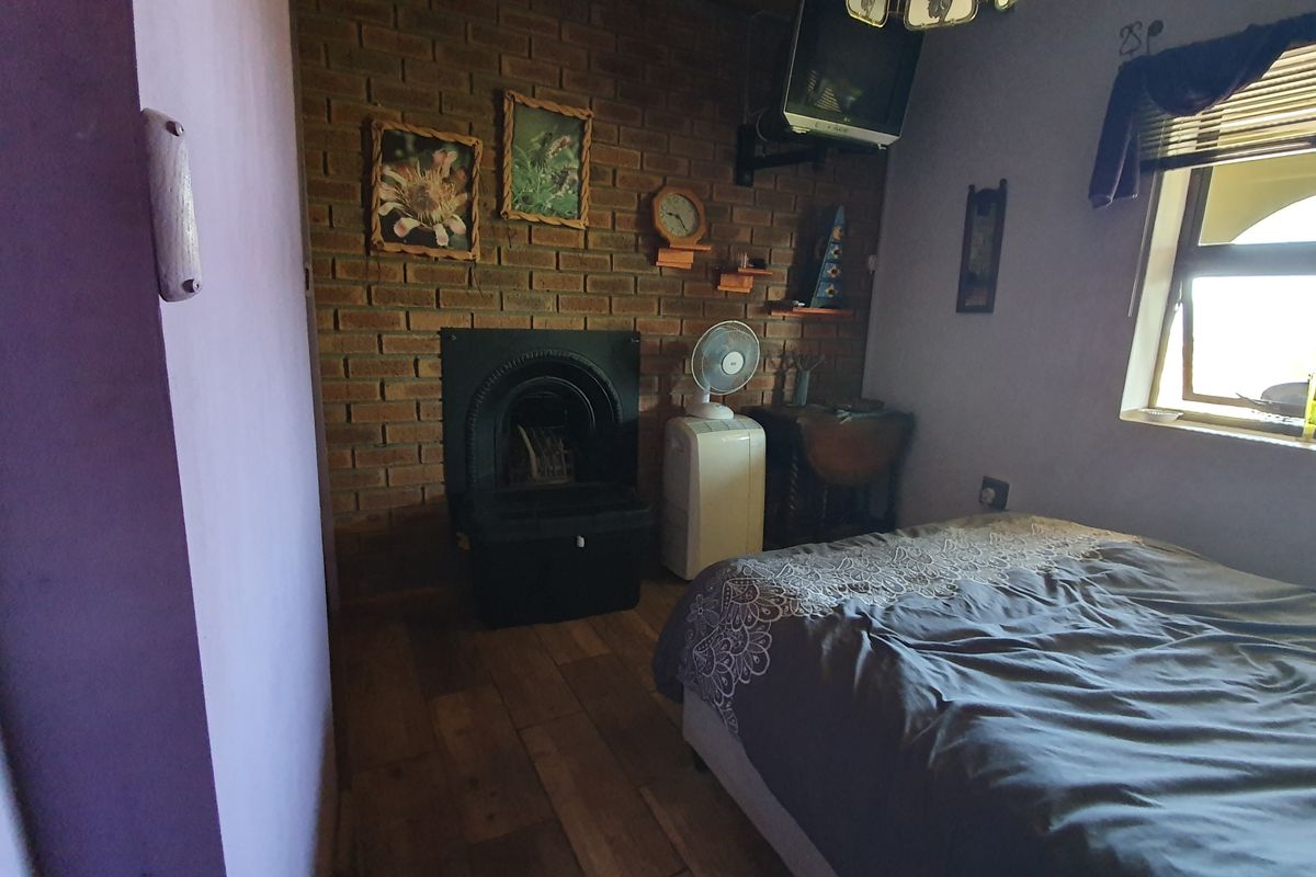 A bedroom featuring an exposed brick wall, a built-in cast iron fireplace, and timber flooring, offering a rustic aesthetic.