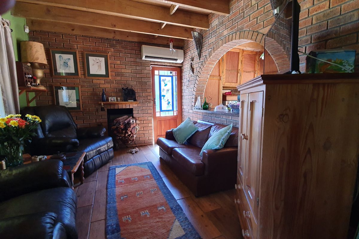Rustic living room featuring exposed brick walls, timber ceiling beams, a brick archway, fireplace, and timber flooring, with an adjacent view into the kitchen area.