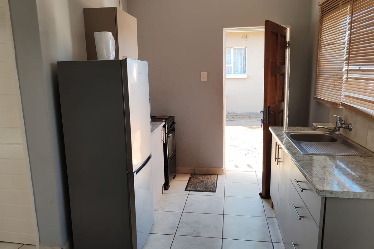 A functional kitchen area featuring tiled flooring, granite-look countertops, a stainless steel sink, and direct access to the exterior.