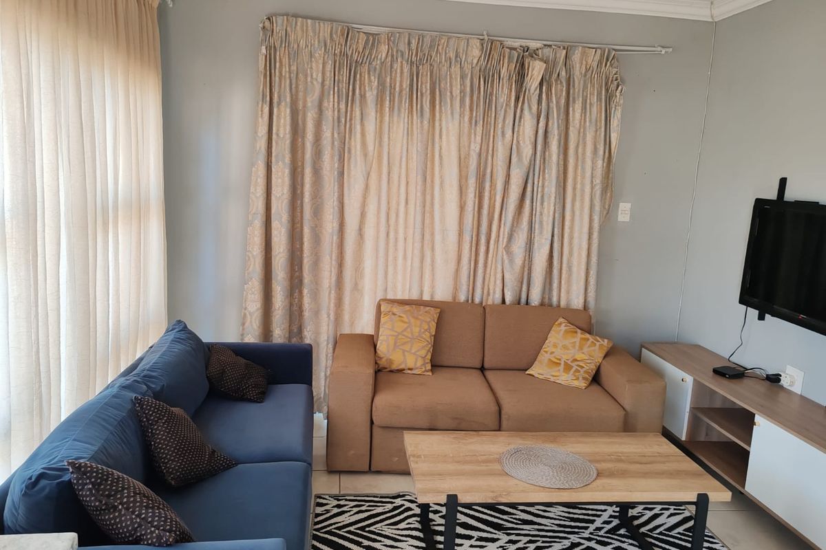 A comfortable living room featuring neutral wall tones, large window treatments, and tiled flooring, providing a functional space for relaxation.