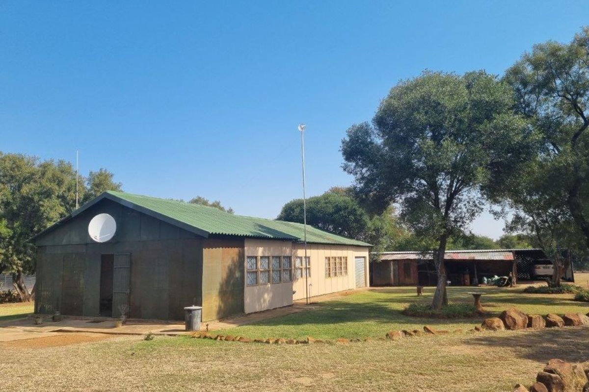 Rear view of a farm property featuring a metal-clad structure with a corrugated roof, set within a spacious garden area with mature trees.