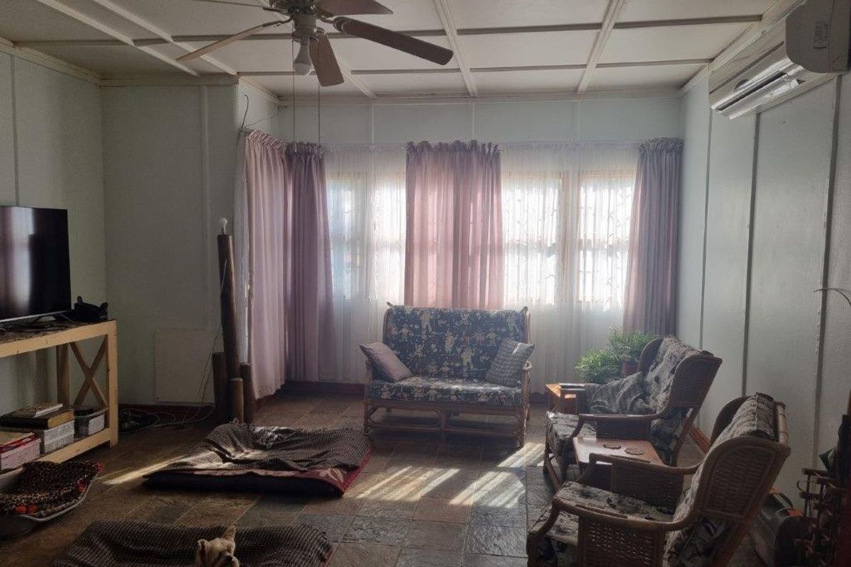 A living room featuring tiled flooring, a coffered ceiling with a fan, and a wall-mounted split-system air conditioner.