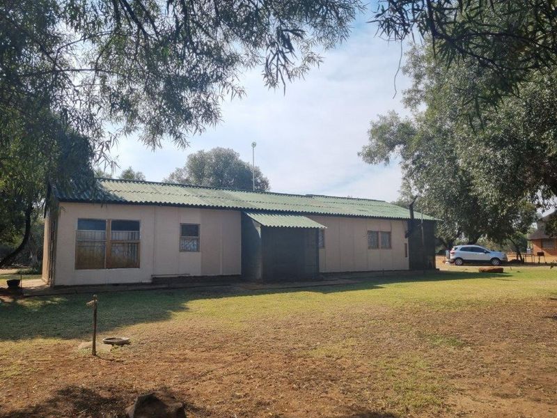 Rear view of a single-story farm dwelling featuring a corrugated metal roof, timber-framed windows with security bars, and surrounding garden space.
