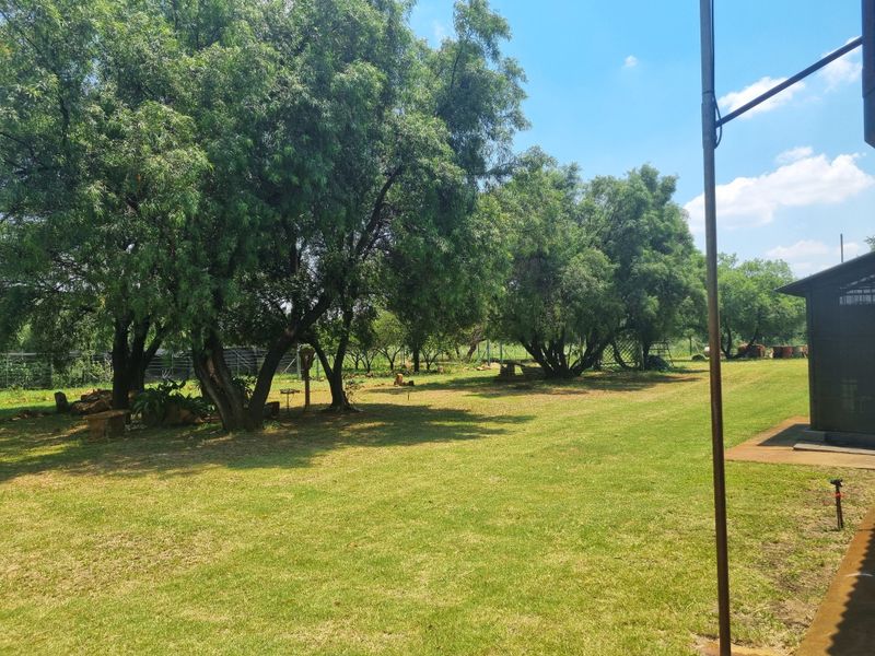 A spacious, well-maintained garden area featuring mature trees, expansive lawn, and perimeter fencing on the farm property.