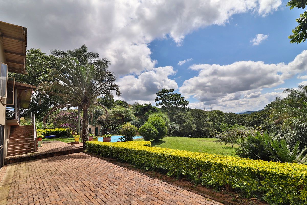 Spacious rear exterior featuring a brick-paved patio, swimming pool, and expansive landscaped garden with mature trees and scenic views.