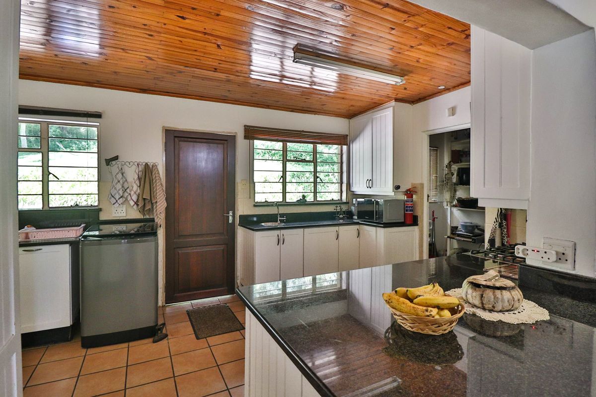 Functional kitchen featuring granite countertops, ample built-in cabinetry, and a distinctive timber-clad ceiling, with an adjacent scullery area.