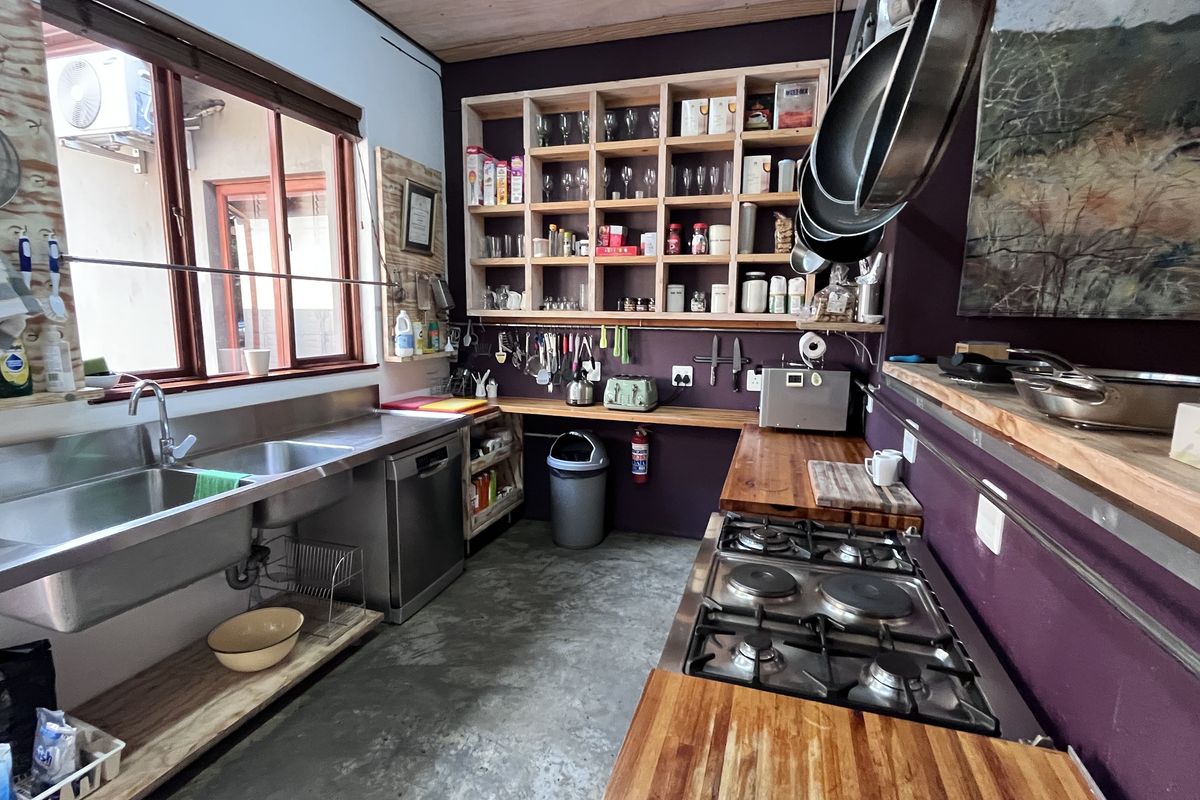 A functional kitchen featuring stainless steel sinks, a built-in gas hob, wooden countertops, and open shelving, set against a dark accent wall.