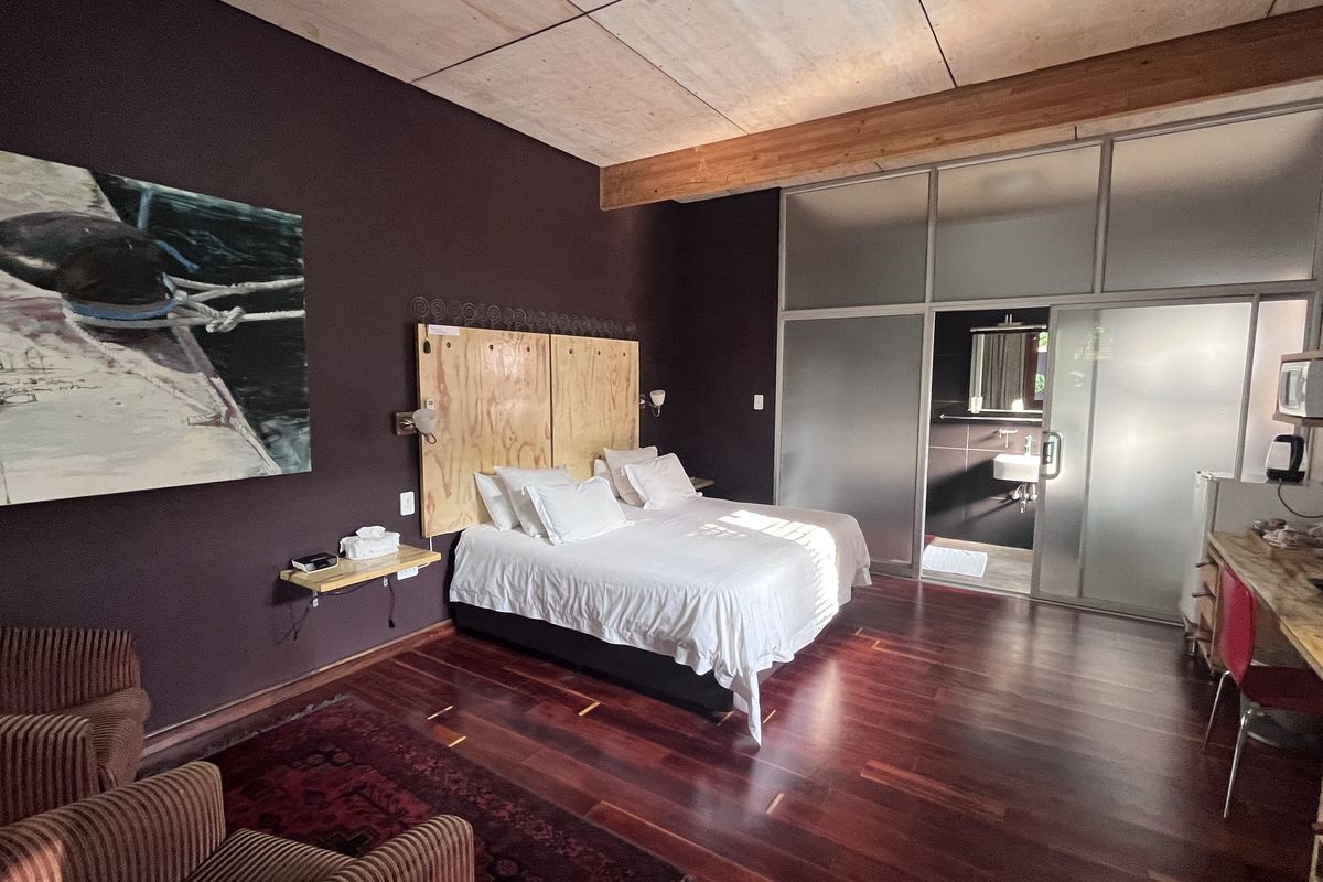A modern bedroom featuring rich hardwood flooring, an exposed timber ceiling beam, and a frosted glass partition leading to an en-suite bathroom.