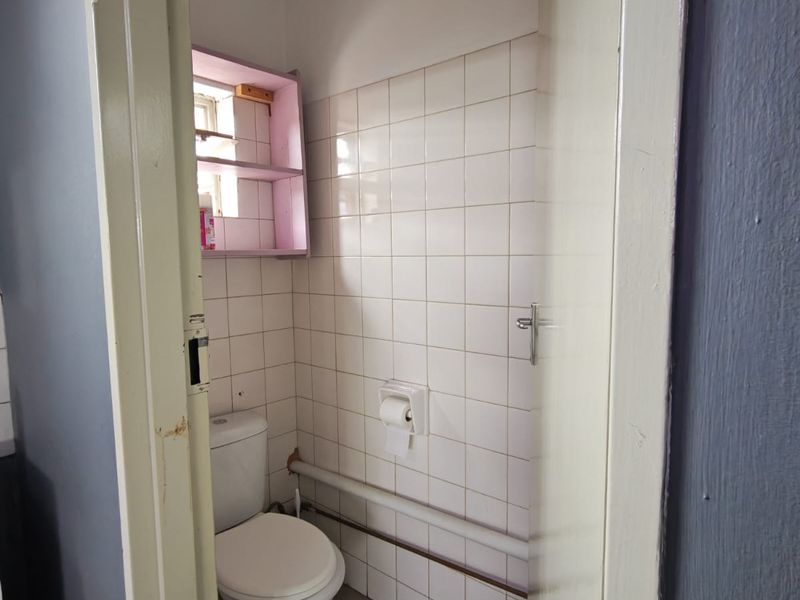 A compact bathroom featuring tiled walls, a standard toilet, and exposed piping, requiring cosmetic updates to improve its overall condition and aesthetic appeal.