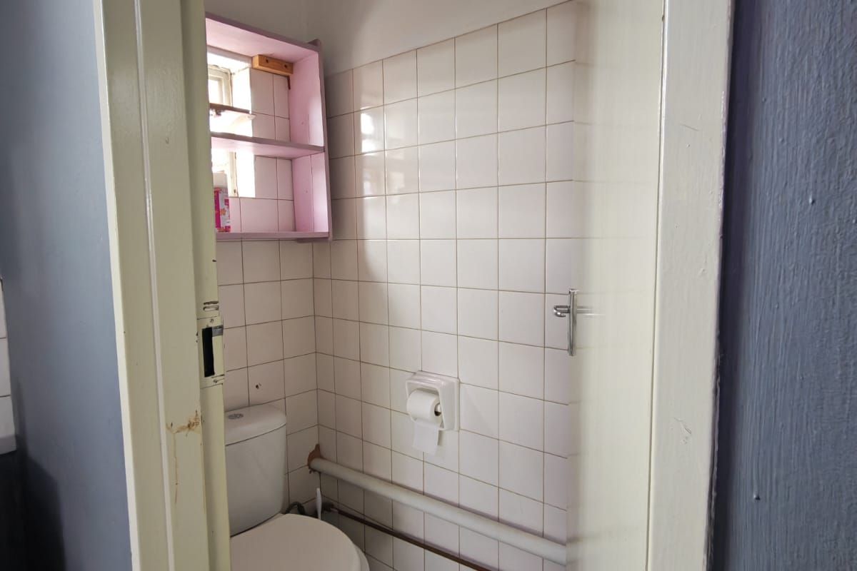 A compact bathroom featuring tiled walls, a standard toilet, and exposed piping, requiring cosmetic updates to improve its overall condition and aesthetic appeal.