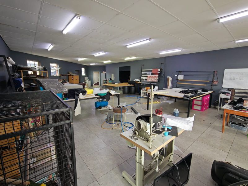 A spacious utility or workshop area featuring tiled flooring, suspended ceiling panels, and industrial fluorescent lighting, suitable for various commercial or production purposes.