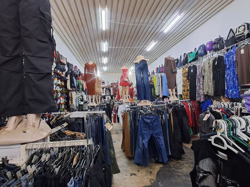 A retail clothing store interior featuring wall-mounted display rails, fluorescent lighting, and a corrugated metal ceiling.