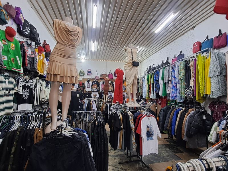 Interior view of a retail clothing store featuring high-density garment racks, mannequins, and industrial-style corrugated metal ceiling with strip lighting.