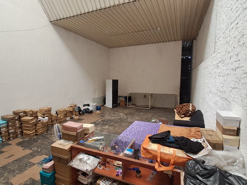 A utilitarian storage or workshop space featuring exposed brick walls, concrete flooring, and a high corrugated metal ceiling.