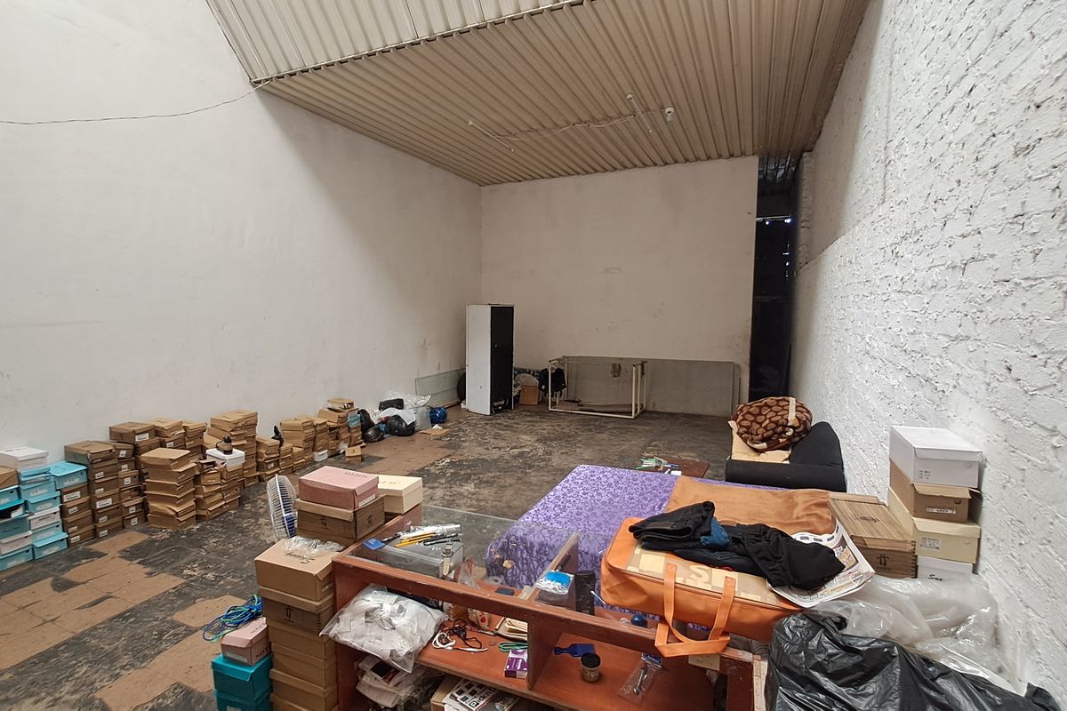 A utilitarian storage or workshop space featuring exposed brick walls, concrete flooring, and a high corrugated metal ceiling.