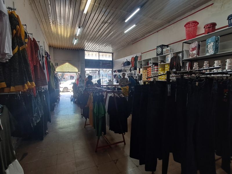 Interior view of a retail shop space featuring tiled flooring, corrugated metal ceiling, and fluorescent lighting, currently utilized for clothing sales.