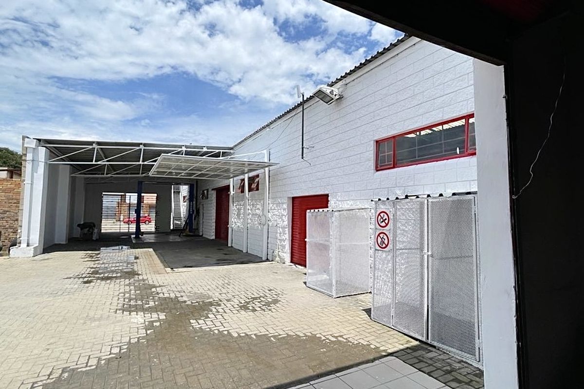 Exterior view of a commercial workshop facility featuring paved yard space, covered work bays, and secure metal storage enclosures.