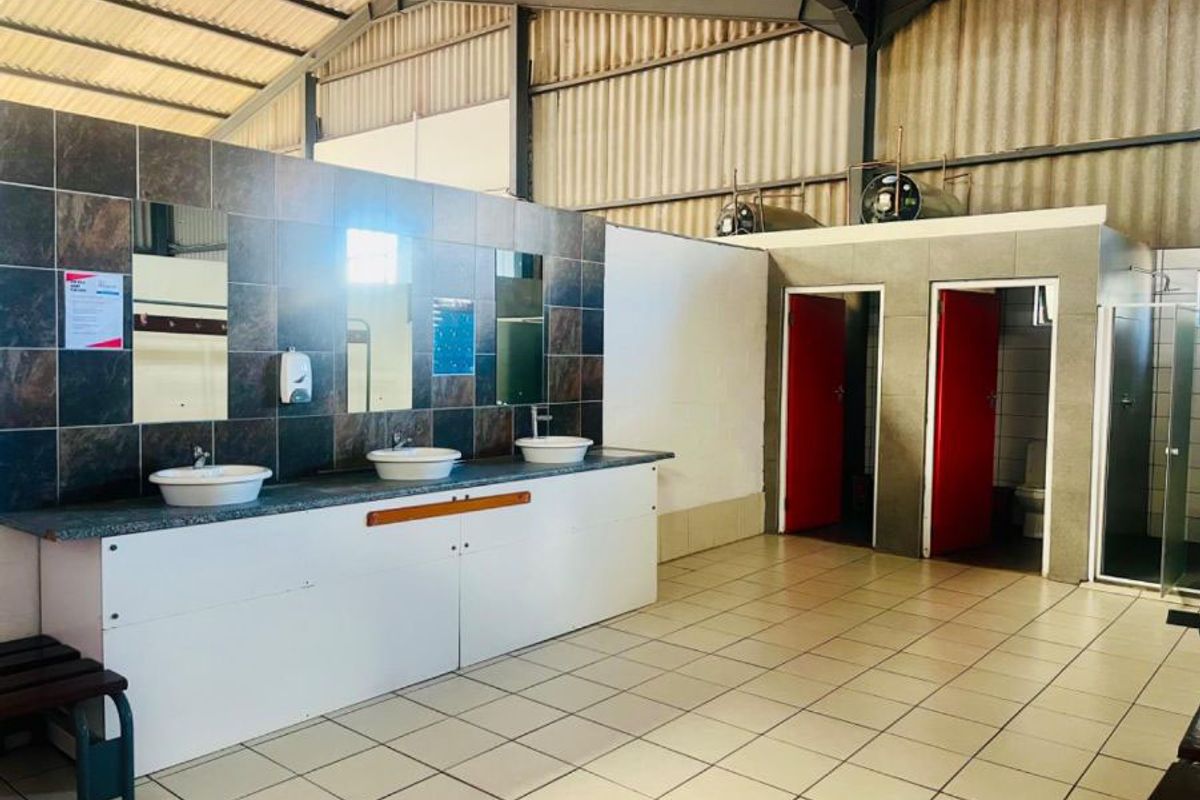 Commercial bathroom facility featuring a long vanity with three vessel sinks, tiled splashback, and multiple private toilet cubicles with red doors.
