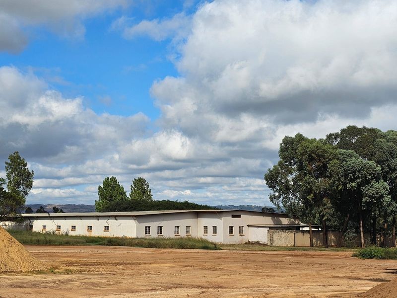 A wide-angle view of the rear industrial building facade, featuring a long structure with multiple windows and a surrounding perimeter wall.