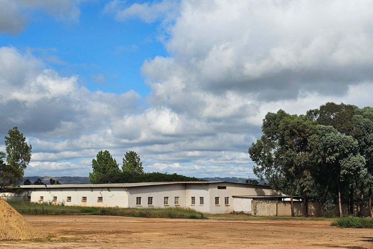 A wide-angle view of the rear industrial building facade, featuring a long structure with multiple windows and a surrounding perimeter wall.
