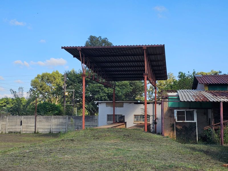 Industrial outdoor area featuring a raised loading platform with a metal canopy structure and surrounding concrete boundary wall.