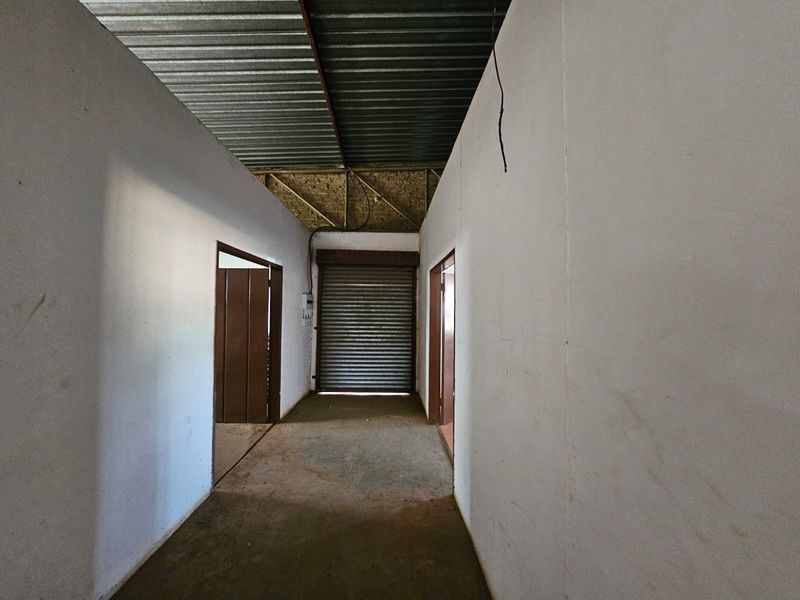 An industrial utility space featuring a corrugated metal roof, exposed trusses, concrete flooring, and a secure roller shutter door.