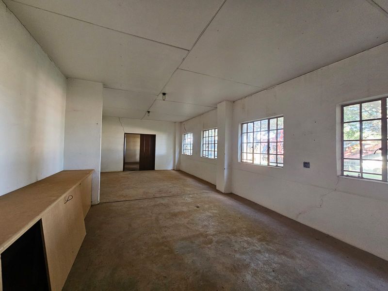 An empty, industrial-style utility space featuring concrete flooring, steel-framed windows, and built-in cabinetry, requiring cosmetic updates to improve its overall condition.