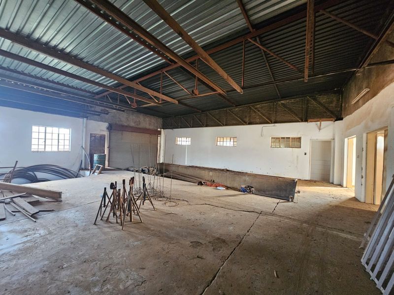Spacious industrial utility area featuring high ceilings with exposed steel trusses, concrete flooring, and a large roller shutter door for easy access.