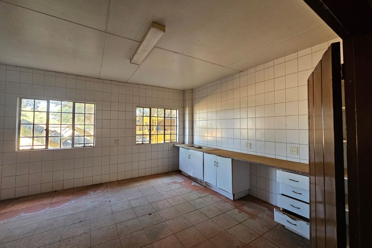A basic industrial kitchen space featuring tiled walls, built-in cabinetry with a sink, and tiled flooring, currently in need of maintenance and refurbishment.