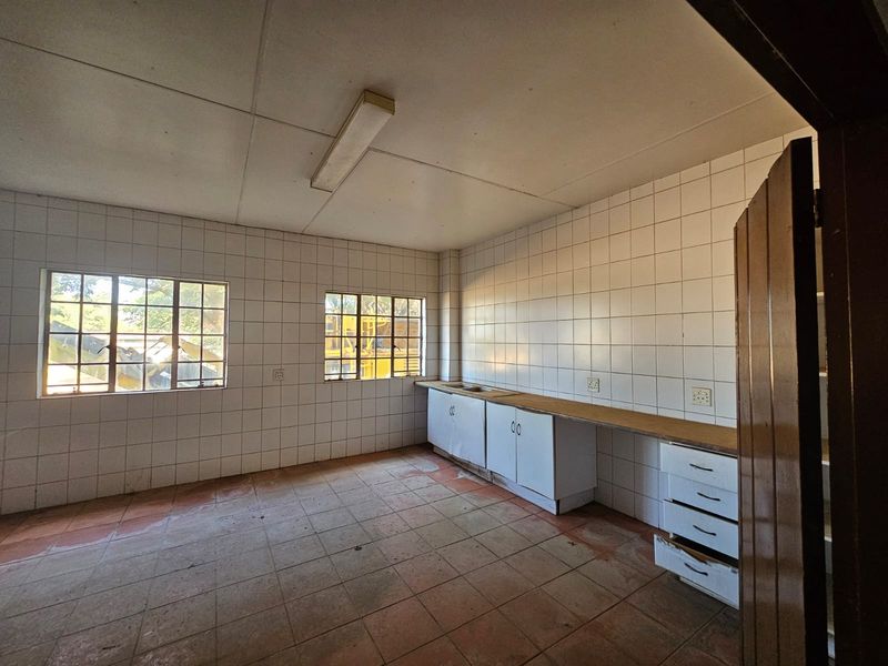 A basic industrial kitchen space featuring tiled walls, built-in cabinetry with a sink, and tiled flooring, currently in need of maintenance and refurbishment.