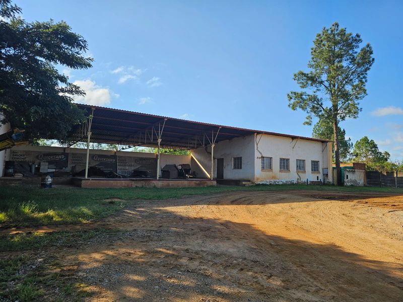 Industrial property featuring a large open-sided metal canopy, raised concrete loading platform, and masonry building structure with security-barred windows.