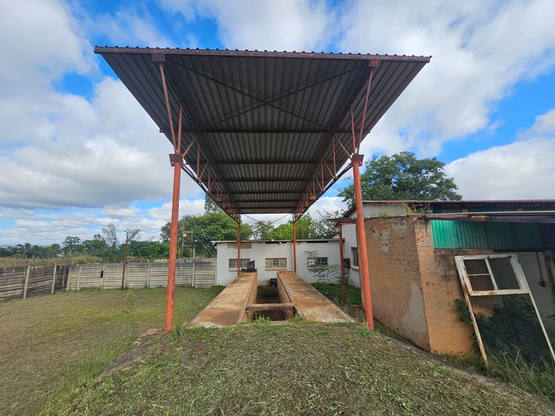 Industrial outdoor area featuring a covered vehicle inspection pit with a metal canopy structure and surrounding brick masonry walls.