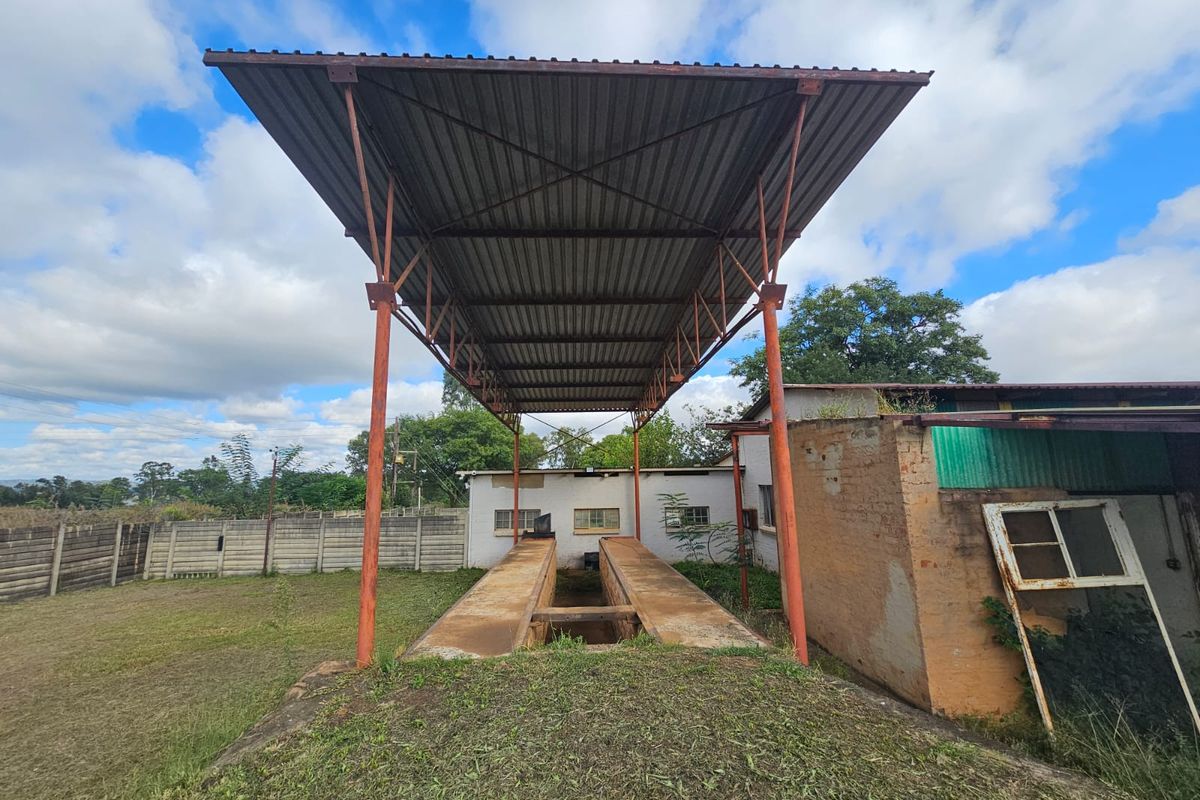 Industrial outdoor area featuring a covered vehicle inspection pit with a metal canopy structure and surrounding brick masonry walls.