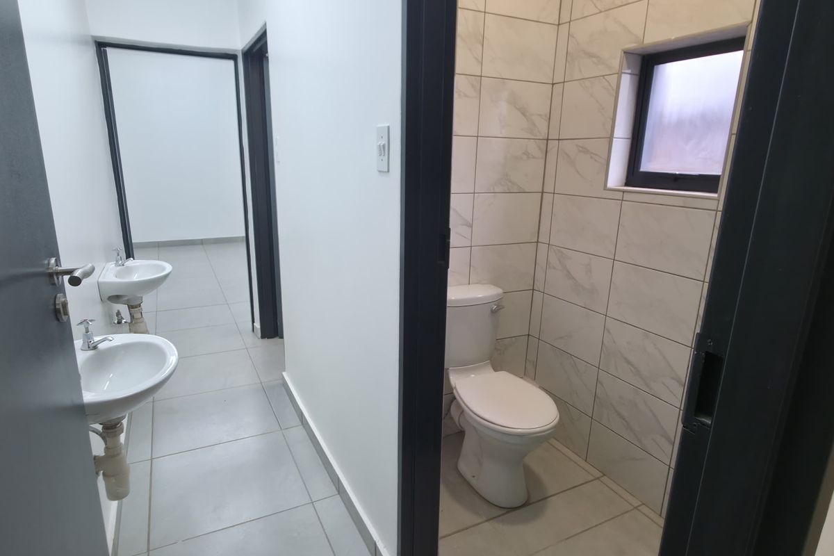 A clean, modern bathroom area featuring two pedestal wash basins in the hallway and a separate enclosed toilet with marble-look wall tiling.