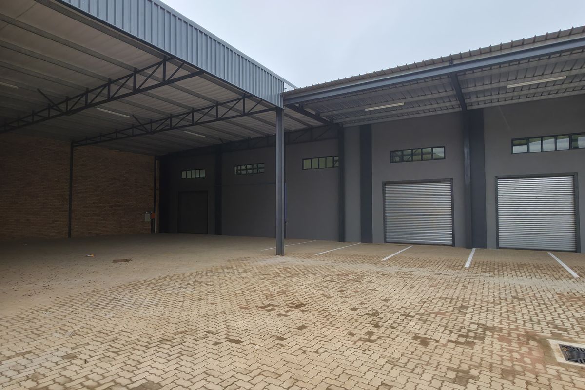 Spacious industrial yard area featuring paved flooring, multiple roller shutter doors, and a covered loading bay with steel structural framing.