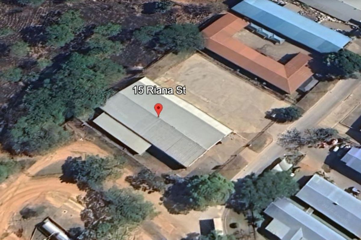Aerial view of an industrial property featuring a large warehouse structure with a metal roof and surrounding yard space.