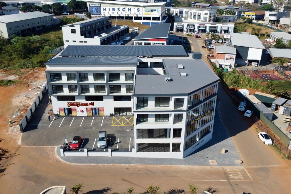 Aerial view of a modern multi-story commercial office building with an adjacent asphalt parking lot and surrounding business park infrastructure.