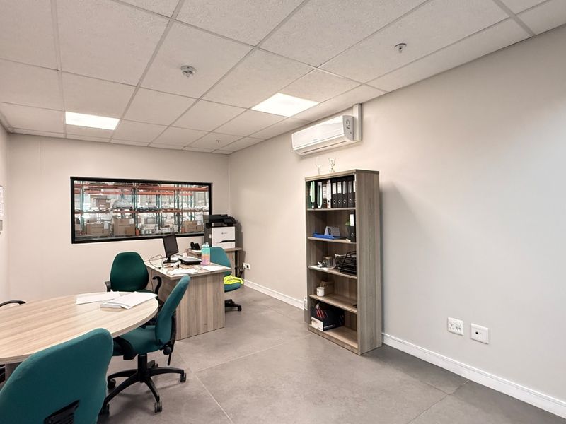 A clean, functional office space featuring tiled flooring, a suspended ceiling with recessed lighting, and a wall-mounted split-system air conditioner.