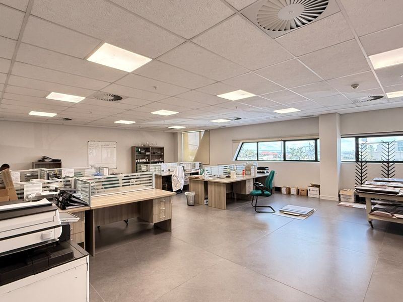Spacious open-plan office area featuring a suspended ceiling with recessed lighting, air conditioning vents, and large windows providing natural light.