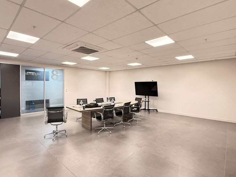 A spacious, modern office meeting room featuring large format floor tiles, a suspended ceiling with recessed lighting, and a glass partition wall.
