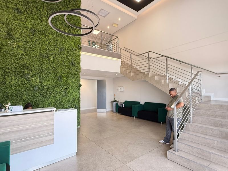 Modern industrial reception area featuring a double-volume ceiling, feature green wall, tiled flooring, and a contemporary staircase with stainless steel balustrades.