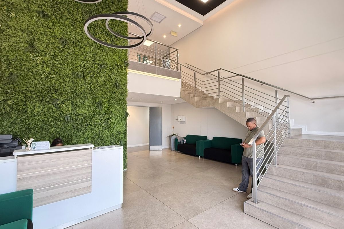 Modern industrial reception area featuring a double-volume ceiling, feature green wall, tiled flooring, and a contemporary staircase with stainless steel balustrades.