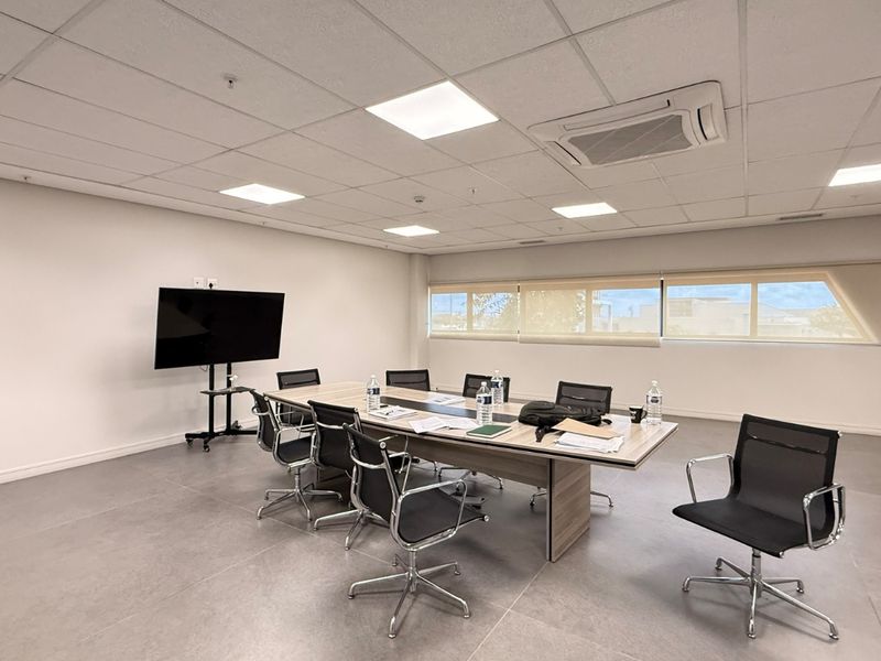 A modern, well-maintained office meeting room featuring tiled flooring, a suspended ceiling with recessed lighting, and a built-in cassette air conditioning unit.