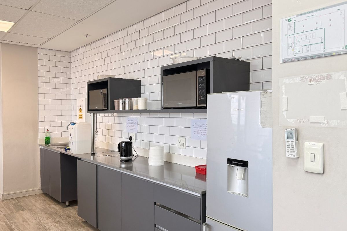A clean, modern industrial kitchenette featuring subway tile backsplash, stainless steel countertops, and grey cabinetry, suitable for office or commercial use.