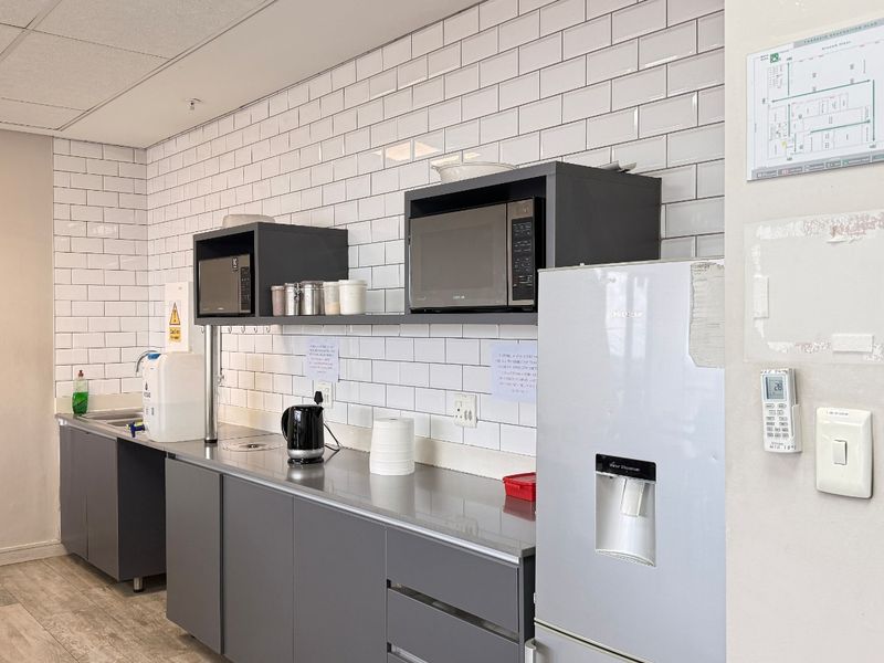A clean, modern industrial kitchenette featuring subway tile backsplash, stainless steel countertops, and grey cabinetry, suitable for office or commercial use.
