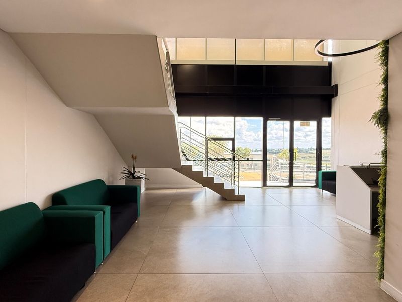 Modern industrial entrance lobby featuring a staircase, large glass windows, tiled flooring, and a built-in reception desk with high ceilings.
